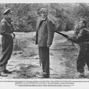 Movie still from Eye of the Needle: a man in a coat is held at gunpoint by two Home Guardsmen during WWII.