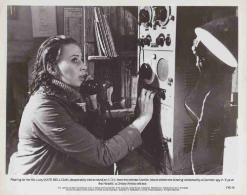 Woman in a turtleneck speaks into a handset while adjusting a vintage radio control panel in a cluttered room (film promo still).