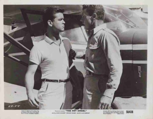 Two men stand beside a small airplane, facing each other in conversation; one in a polo shirt, the other in a uniform.