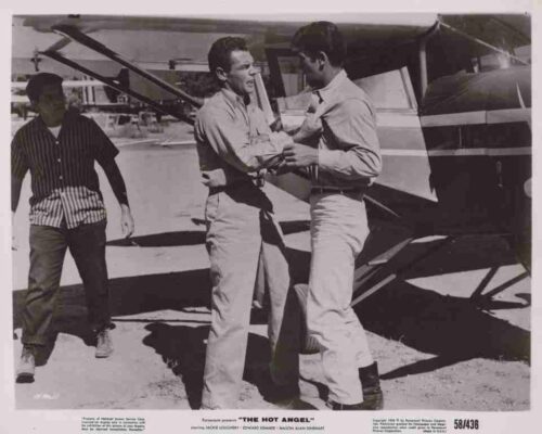 Movie still: two men shake hands at a small airplane on a tarmac, with a third man nearby; vintage 1950s vibe for 'The Hot Angel'