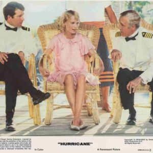 Three people sit in wicker chairs on a sunlit porch: a woman in a pink dress between two men in white naval uniforms, chatting.