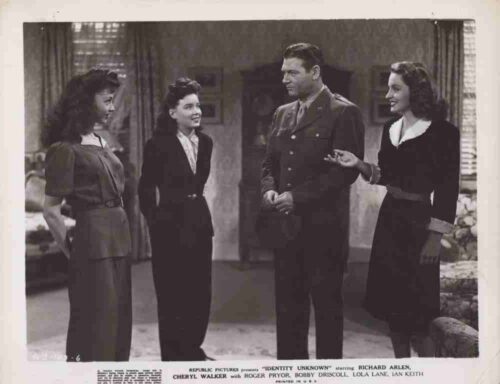 Four adults in vintage attire stand in a living room, with a man in a military uniform center, conversing with three women.