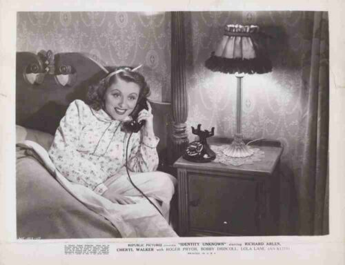 Woman in a floral nightgown sits up in bed, talking on a vintage corded telephone beside a lit bedside lamp and dark wood nightstand to the right.