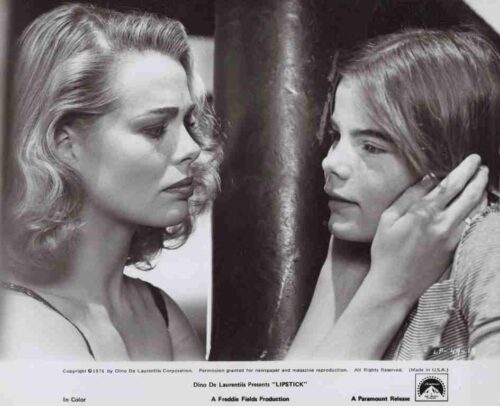 Black-and-white film still of two women standing close by a pillar, one gently cupping the other’s ear.