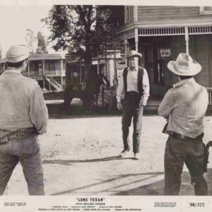Three cowboys in a dusty Western town square; two gunfighters with holsters face a man in a hat near a bank storefront.