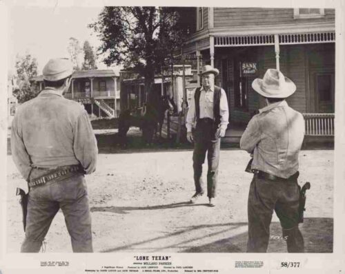 Three cowboys in a dusty Western town square; two gunfighters with holsters face a man in a hat near a bank storefront.