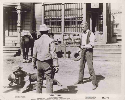 Western town street scene: a man with a hat and pistol stands over a kneeling man while another man lies on the ground; a horse and wooden buildings are in the background.