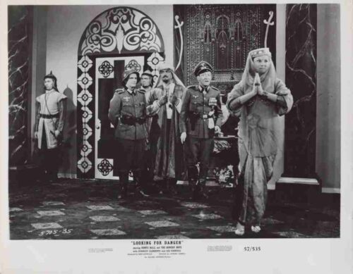Staged black-and-white scene: military officers in uniform with a robed woman praying in a grand hall; a guard stands on the left; caption reads 'Looking for Danger'.