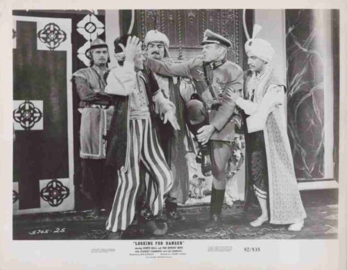 Stage scene with actors in period costumes; a uniformed officer holds back a striped-pants man as others look on, dramatic confrontation on set.