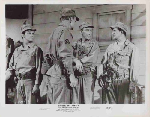 Black-and-white photo of four soldiers in uniform standing and talking outside a building.