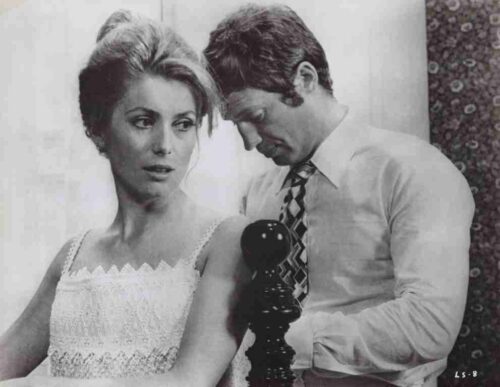 Black-and-white photo of a woman in a lace dress and a man in a shirt and tie standing beside a vintage rotary phone on a stand.