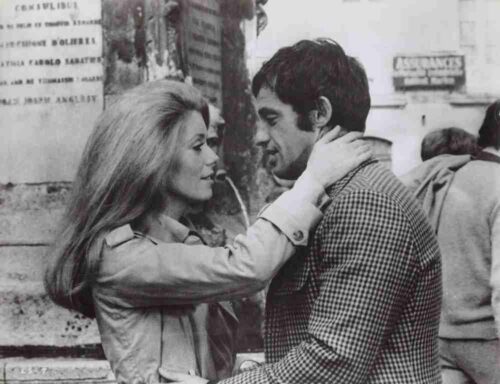 Woman with long hair holding a man's neck in a street embrace, both looking at each other affectionately in a black-and-white photo.